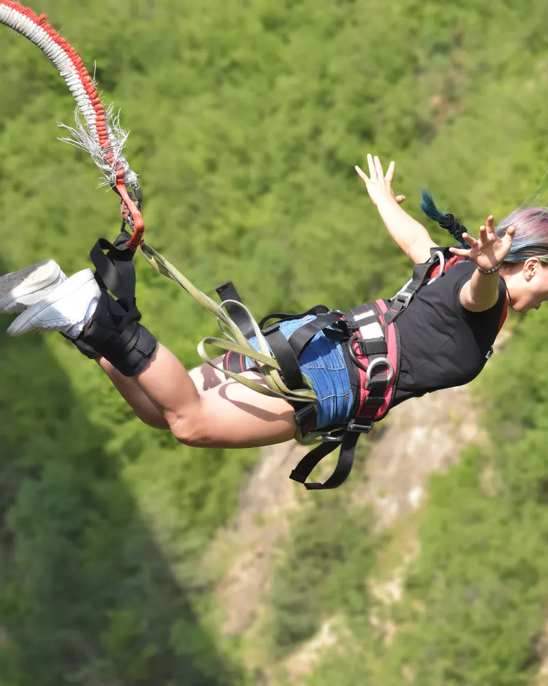 Bungee jumper mid-fall above a forested gorge