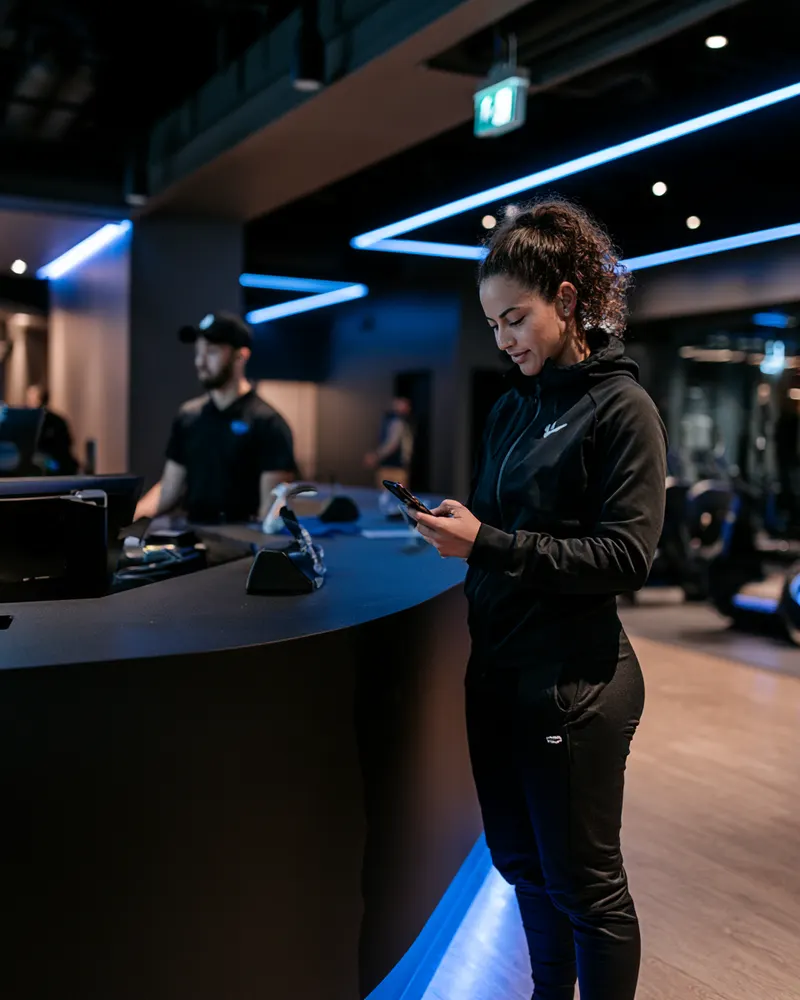 Member checking in on her phone at a modern gym front desk
